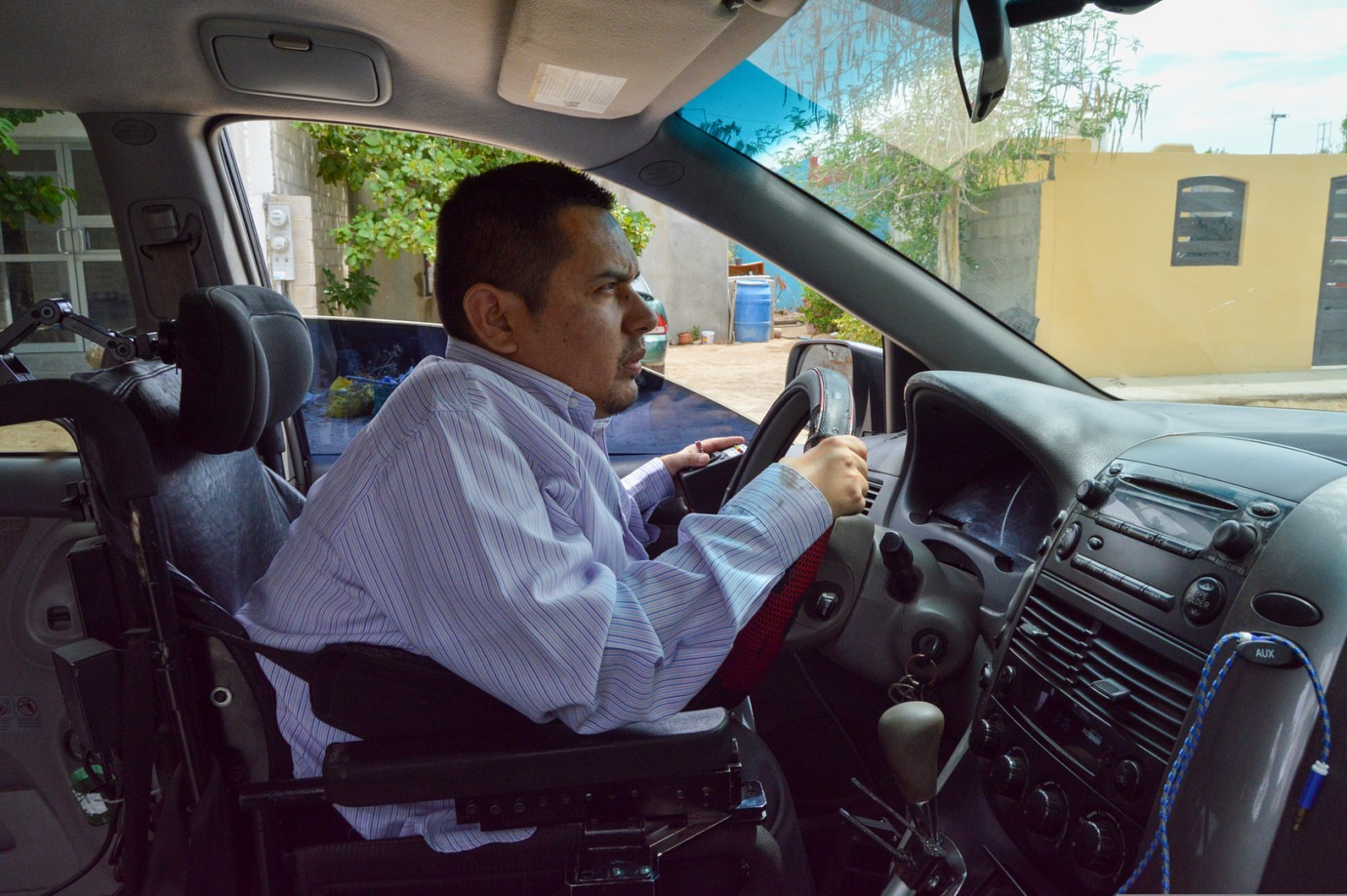 b. José Olin al volante en su silla de ruedas tomando el volante y un joystick